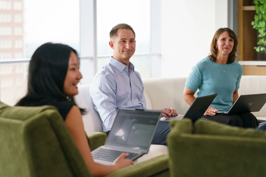 Three NISA colleagues with laptops talking in a bright office lounge